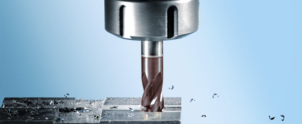 Primer plano de una broca de metal acoplada a una máquina, perforando activamente una superficie metálica, con virutas de metal esparcidas alrededor sobre un fondo azul claro.